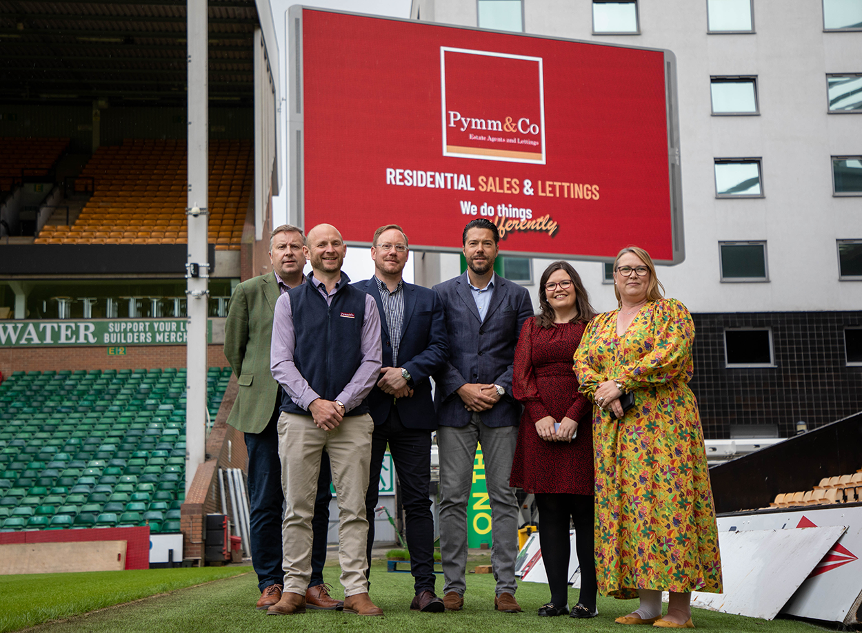 The Pymm & Co Sales and Lettings team standing in front the Pymm & Co brand takeover on the big screen at Norwich City Football Club