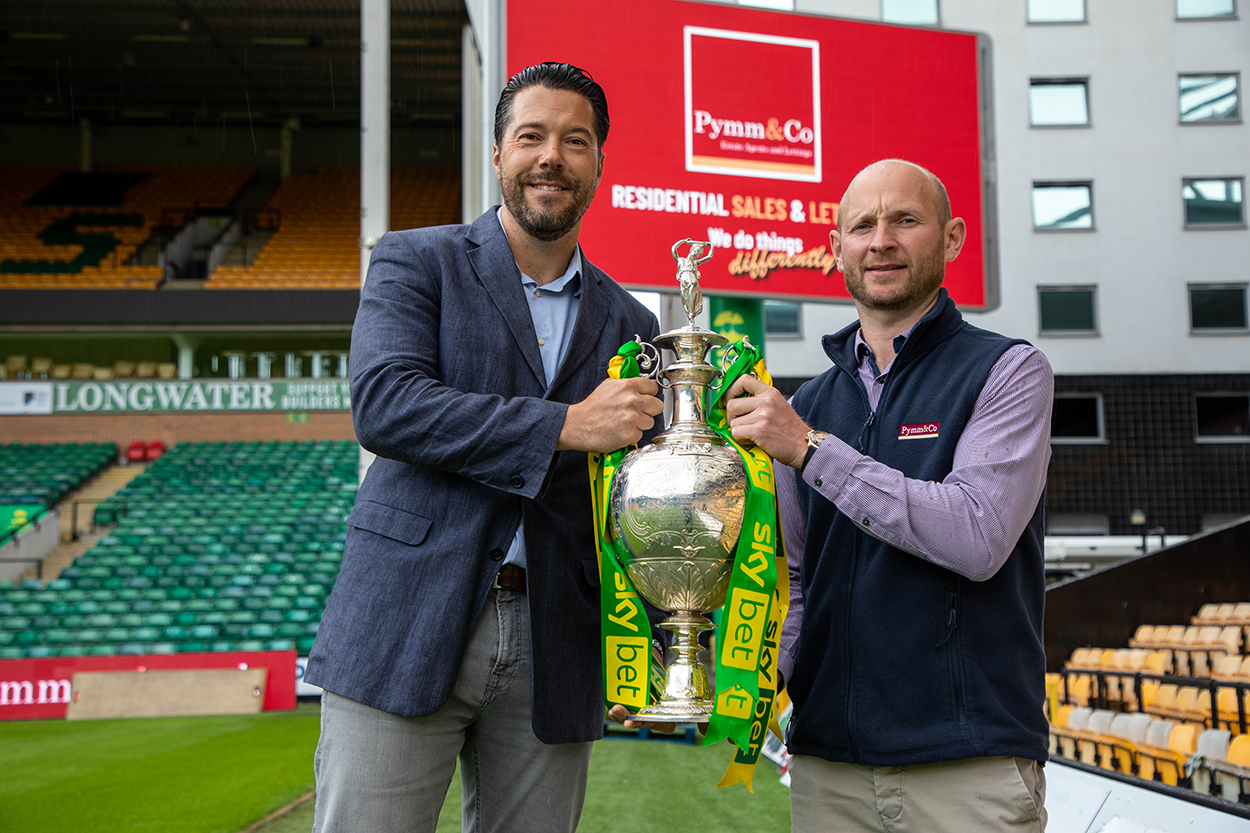 Steve Pymm and Stuart Monument standing in front of the big screen brand takeover at Norwich City Football Club.